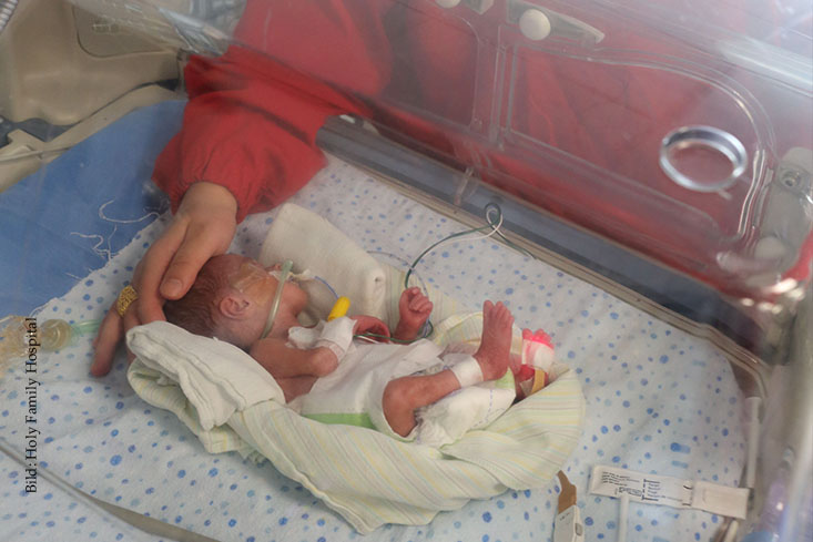Eine Hand streichelt Kopf von Baby in Inkubator